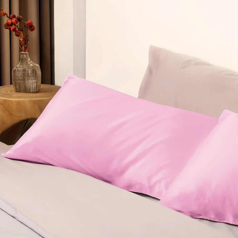 A pink satin pillowcase with an envelope closure resting on a light-colored bed.