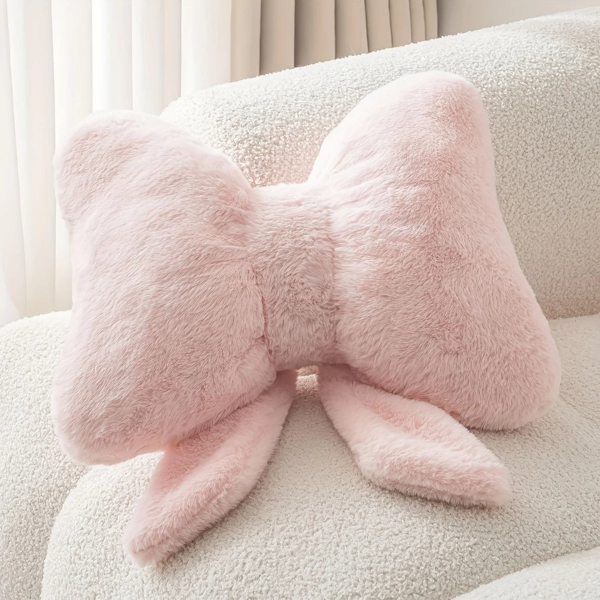 A fluffy pink decorative bow pillow resting on a white textured surface.