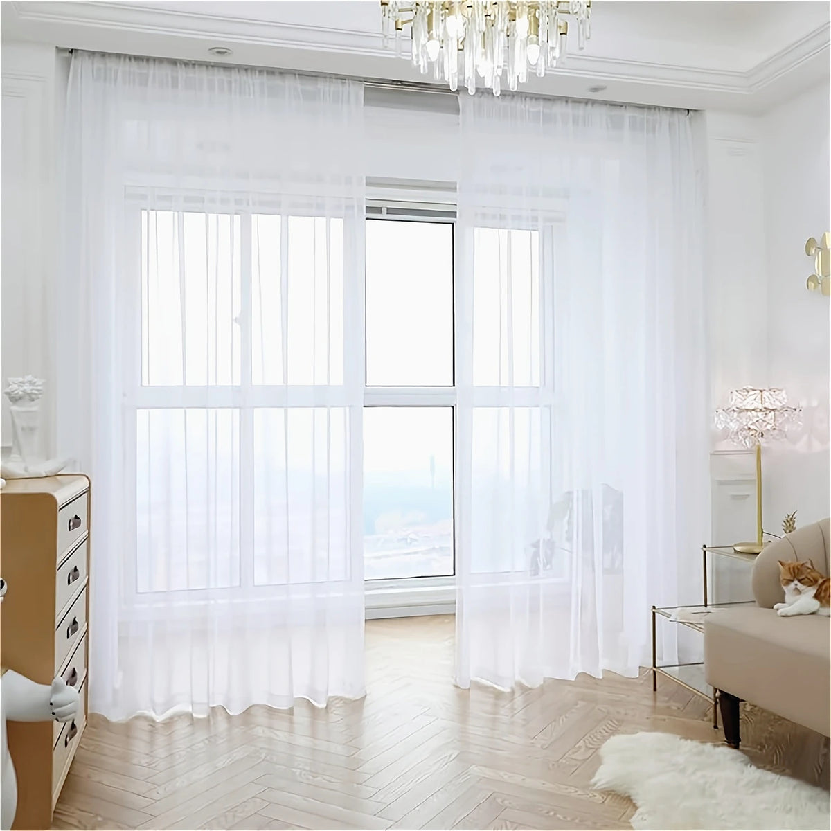 White semi-sheer tulle curtains covering a large window with natural light and wooden flooring.