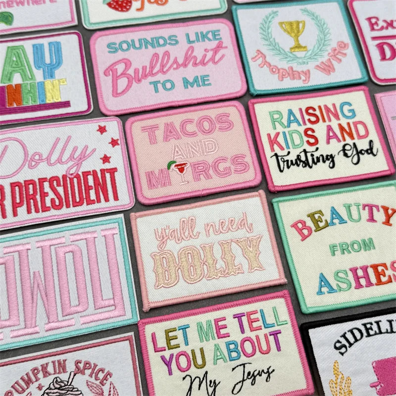 A collection of pink and green embroidered slogan patches featuring phrases like Bullshit to me, Tacos and Margs, and Dolly P