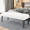 A white bench with dark legs and a gray striped rug placed in front of a wooden bed.