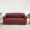 A deep burgundy PU leather sofa slipcover placed on a light rug in a bright room.