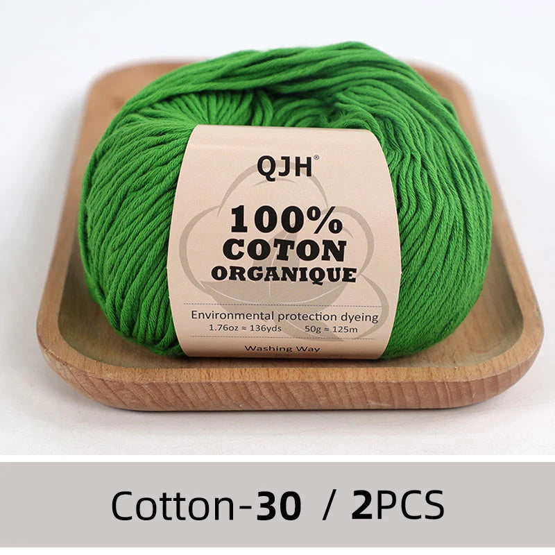 A ball of bright green 100% organic cotton yarn is displayed on a wooden tray.