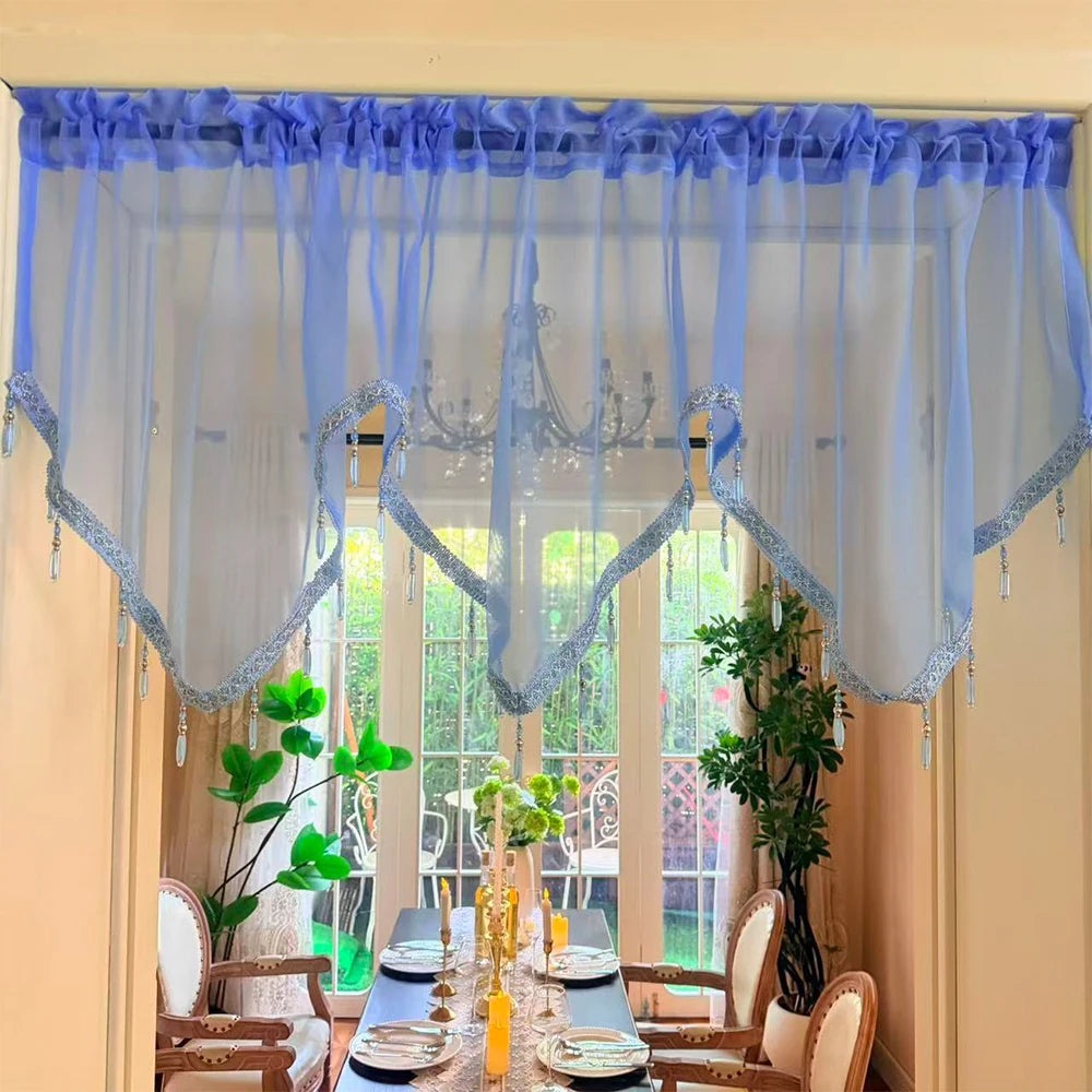 A sheer blue and gray beaded curtain with tassels hangs over a window, framing a dining table.