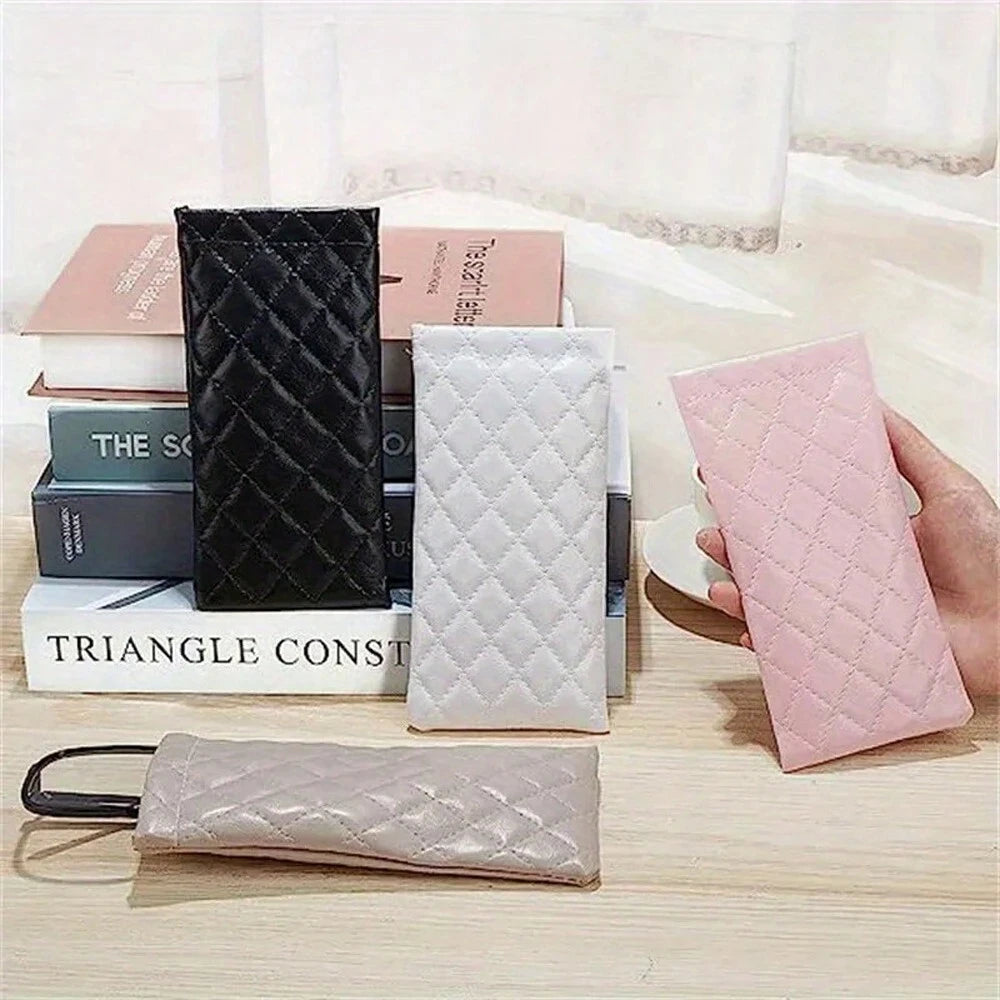 A collection of quilted PU leather eyeglass cases in black, white, and pink are displayed on a wooden surface.