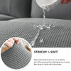A hand pours liquid onto a gray textured sofa fabric, demonstrating the waterproof and soft nature of the slipcover.