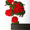 Red embroidered rose flower patches with green leaves on a white background