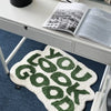 A natural fiber foot mat with a textured surface featuring a repeating pattern of green letters on a white background.