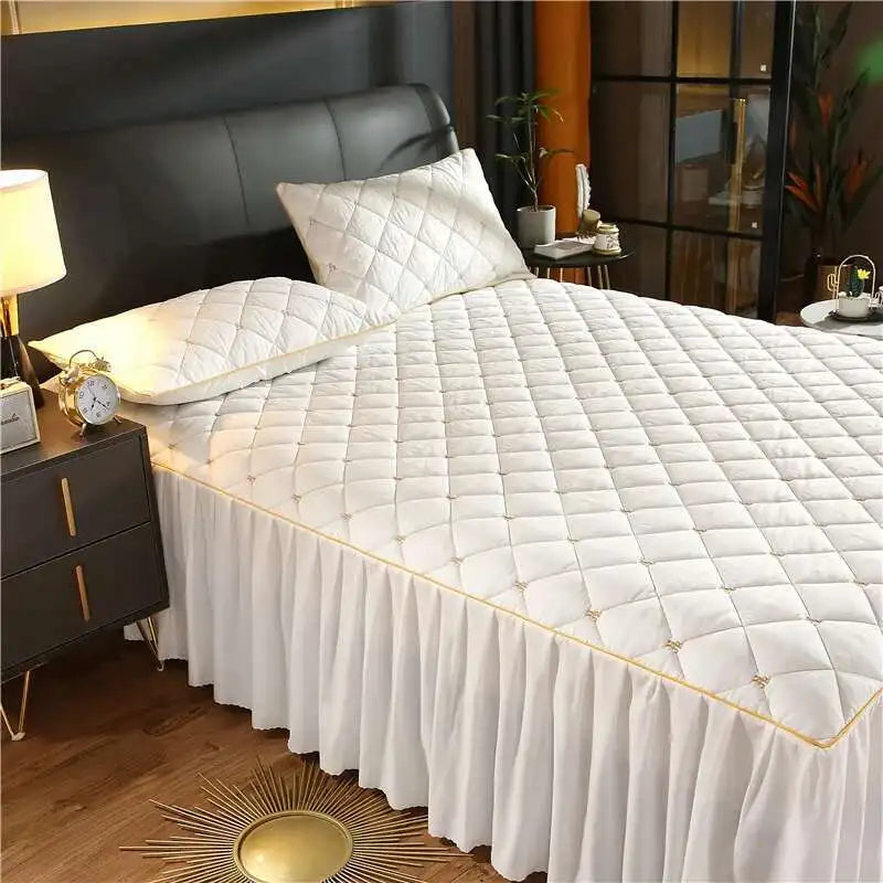 White quilted bed skirt with gold trim covering a queen mattress.