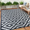 A black and white geometric outdoor rug placed on a wooden deck with greenery in the background.