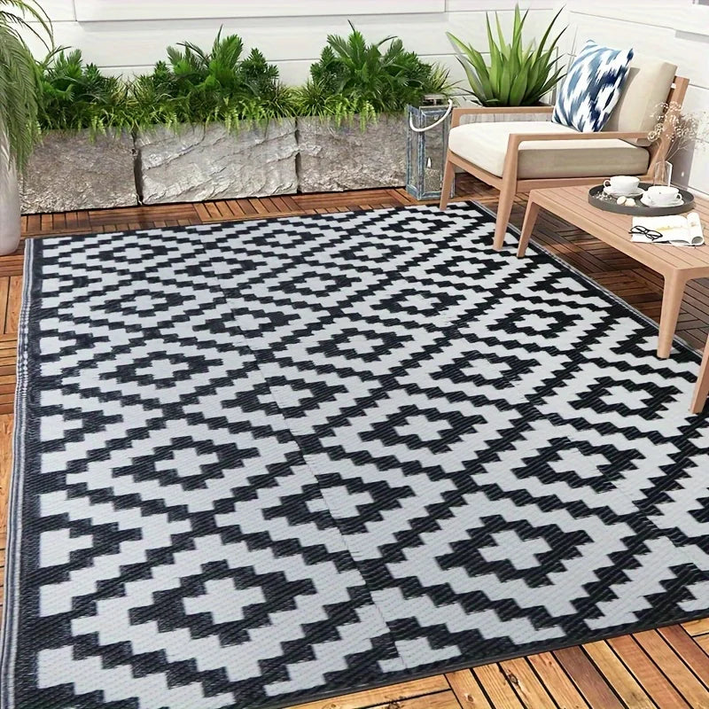 A black and white geometric outdoor rug placed on a wooden deck with greenery in the background.