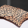 Two leopard print silk satin pillowcases in a beige and black pattern are shown folded on a white surface.