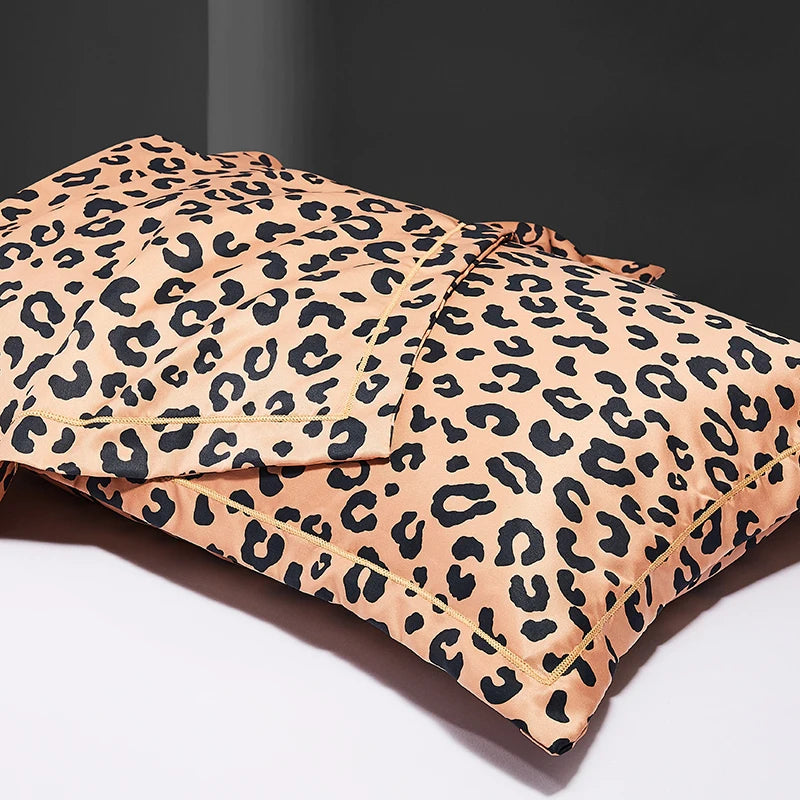 Two leopard print silk satin pillowcases in a beige and black pattern are shown folded on a white surface.