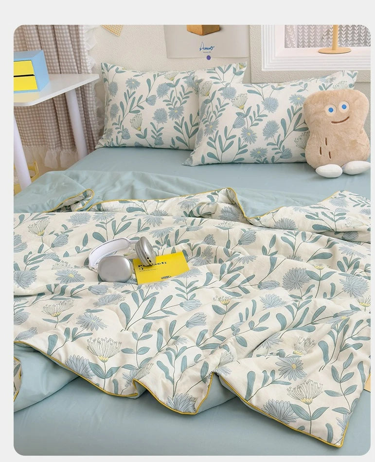 A light blue summer gauze cotton quilt with a floral pattern and a small stuffed animal on a bed.