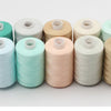 A row of ten spools of 10-color polyester sewing thread in various pastel shades.