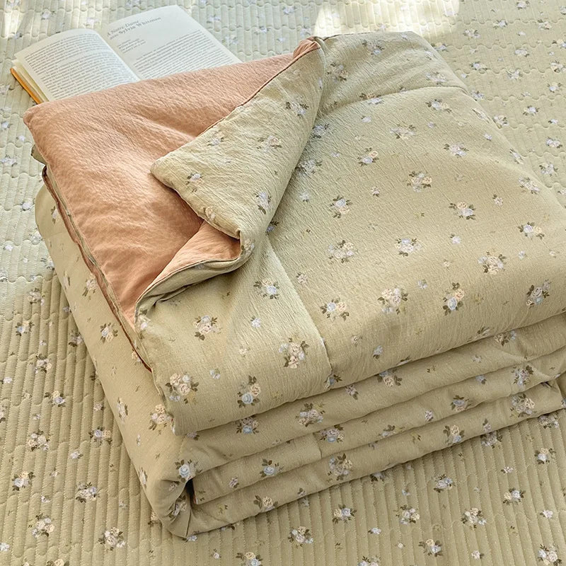 A stack of light beige cartoon quilting comforters and a book on a textured fabric surface.