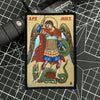 An embroidered patch depicting the Archangel Michael with wings, holding a sword, and standing over a serpent.