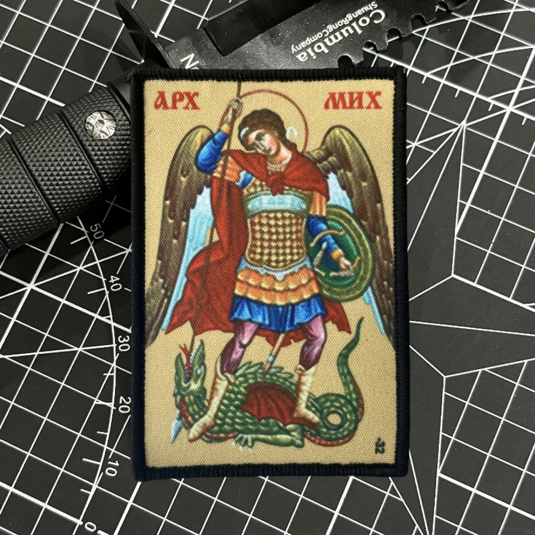 An embroidered patch depicting the Archangel Michael with wings, holding a sword, and standing over a serpent.