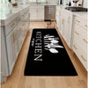 Black non-slip flannel area rug with the word KITCHEN written in white text placed on a light wood floor.