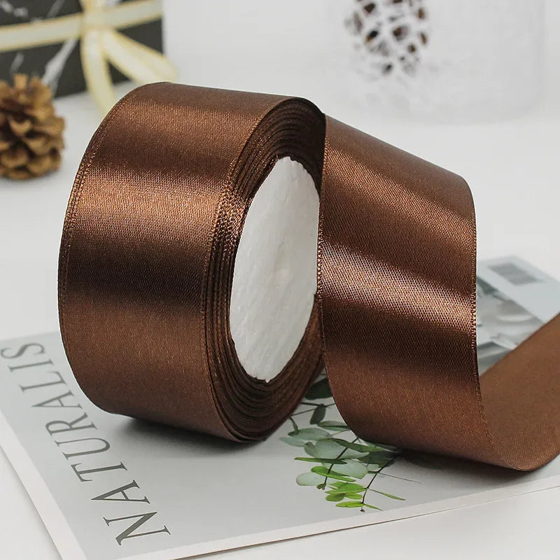 A roll of satin craft ribbon in a rich brown color is shown lying on a piece of paper.