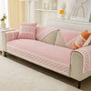 A pink quilted sofa cover with lace trim and beige fabric is displayed on a light-colored sofa.