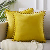 A bright yellow velvet decorative cushion cover with gold stud trim resting on a light gray sofa.