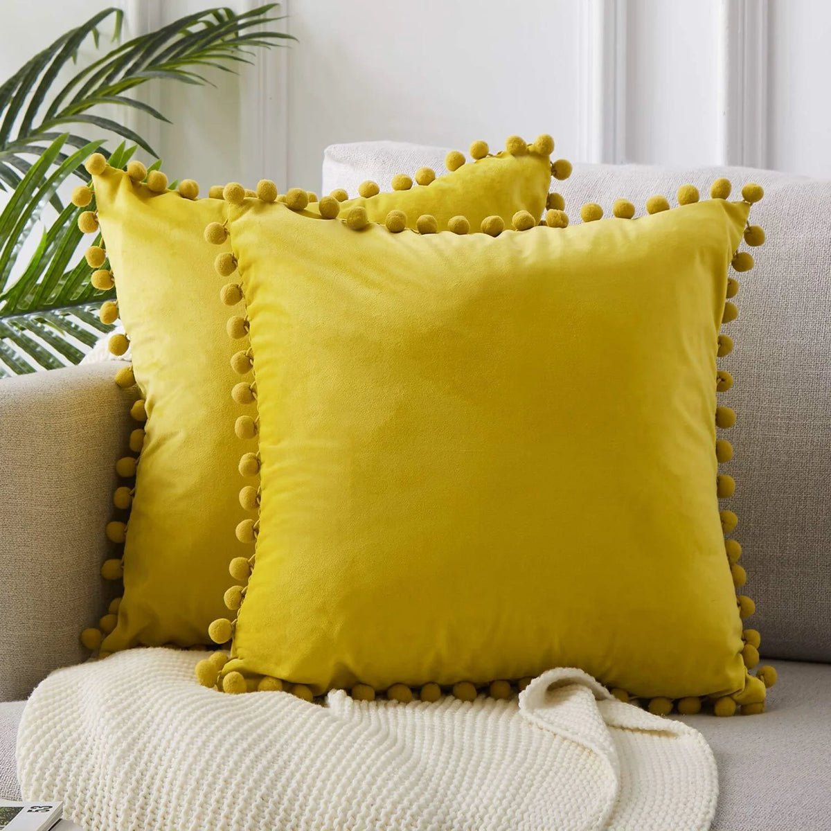 A bright yellow velvet decorative cushion cover with gold stud trim resting on a light gray sofa.