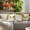 A set of decorative throw pillow covers featuring golden and white feather patterns on a neutral sofa.
