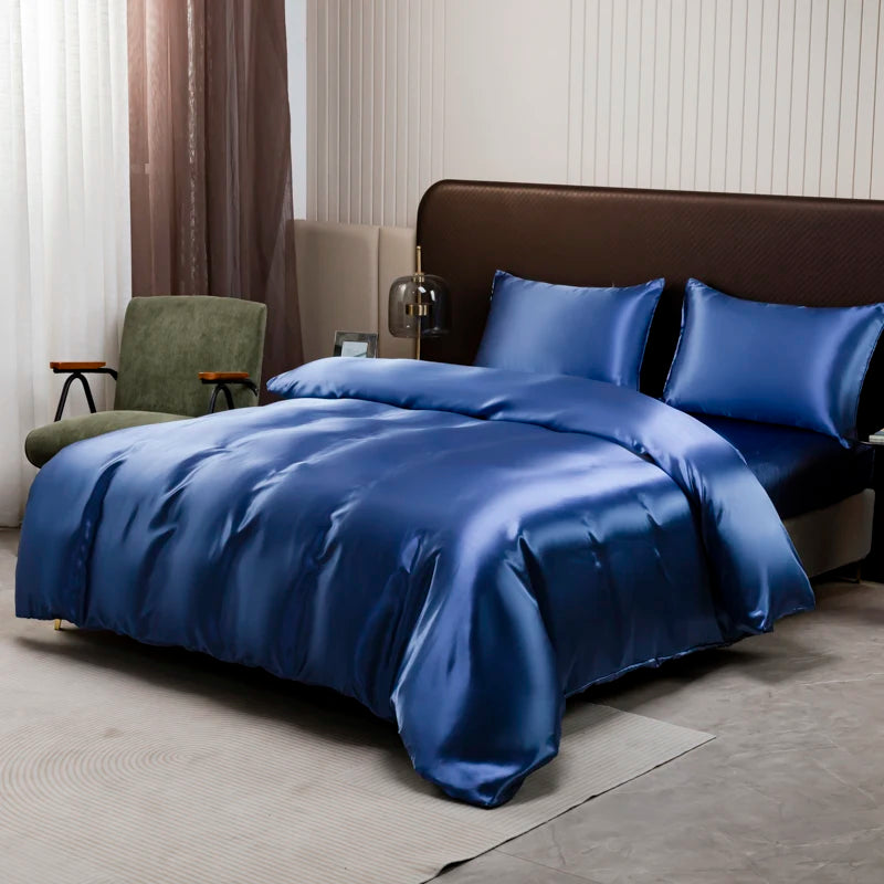 A deep blue satin duvet and pillow set displayed on a bed with brown upholstery and sheer curtains.