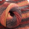 A ball of multi-colored wool yarn featuring shades of orange, red, and brown is shown on a knitted fabric.
