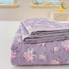 A stack of lavender floral quilted bedspreads folded neatly on a white surface.