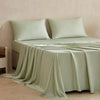 A light sage green bamboo fiber flat bed sheet draped over a bed, showing its smooth texture.
