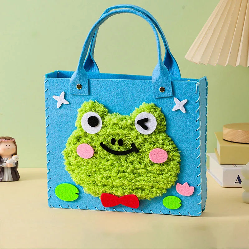 A bright blue felt bag featuring a green frog design with large eyes and a smiling mouth.