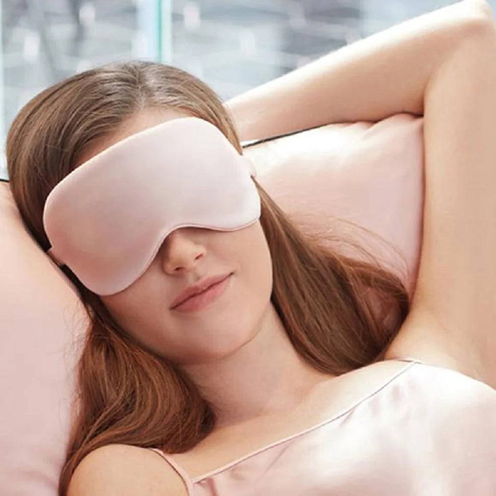 A woman is wearing a pink silk sleep mask while relaxing.