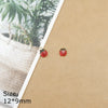 A pair of red ladybug resin charms with gold-colored jump rings displayed on brown paper.