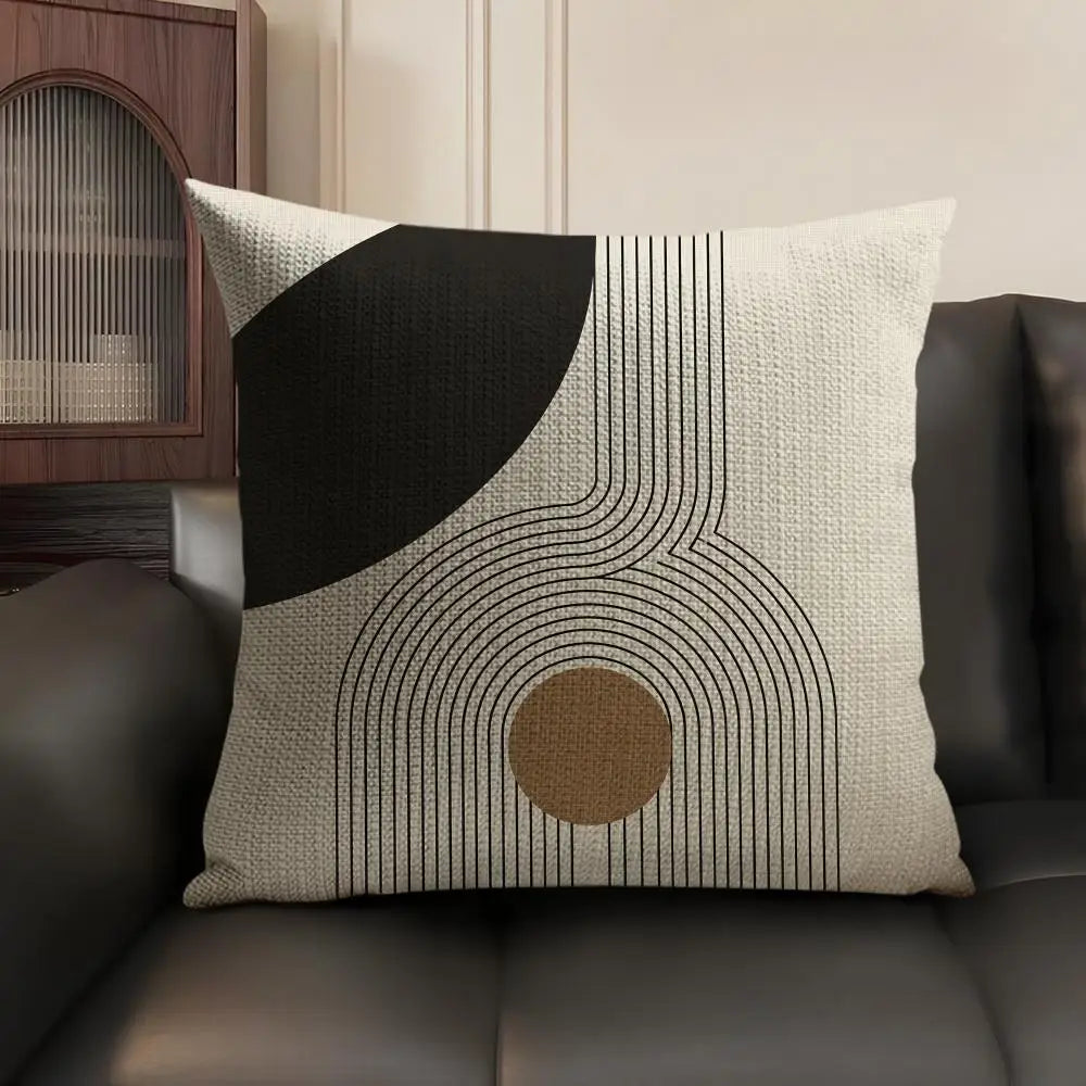 A beige cushion cover with black geometric lines and a circular accent on a dark leather sofa.