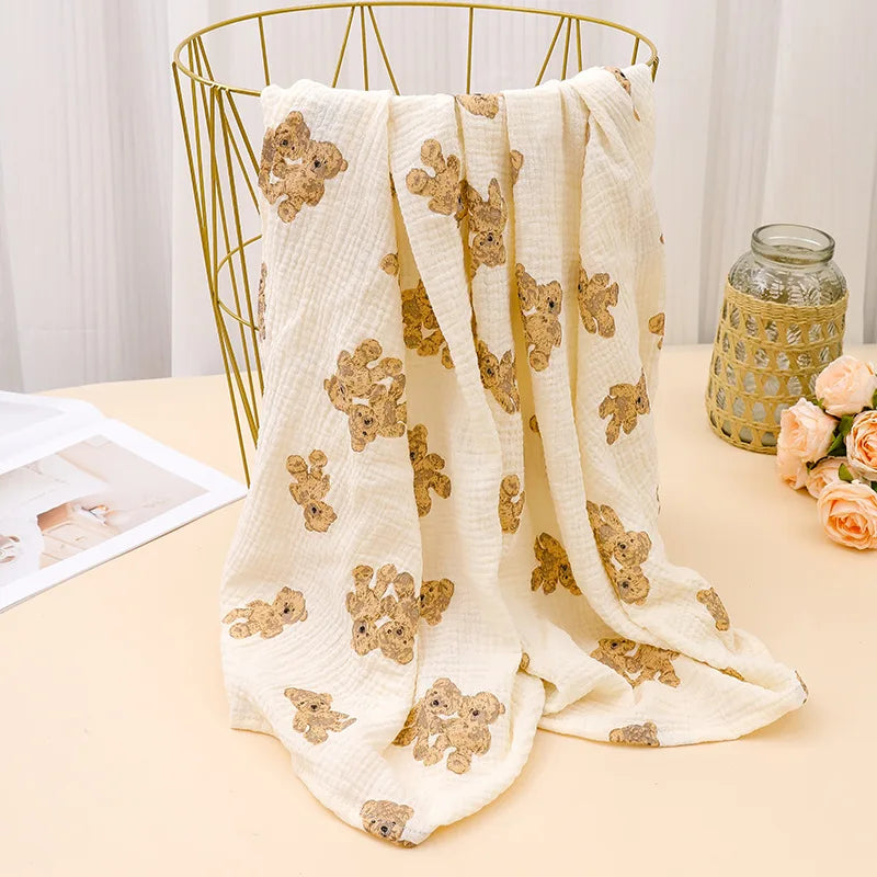 A bundle of cream-colored printable cotton crib sheets featuring a pattern of gold-toned woodland animals on a light wooden s