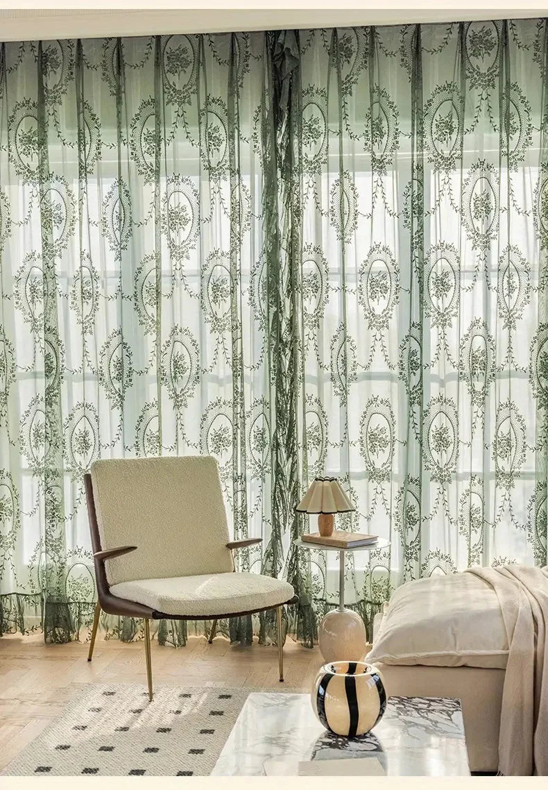 Sheer floral lace curtain panels in green and white hanging in a window.