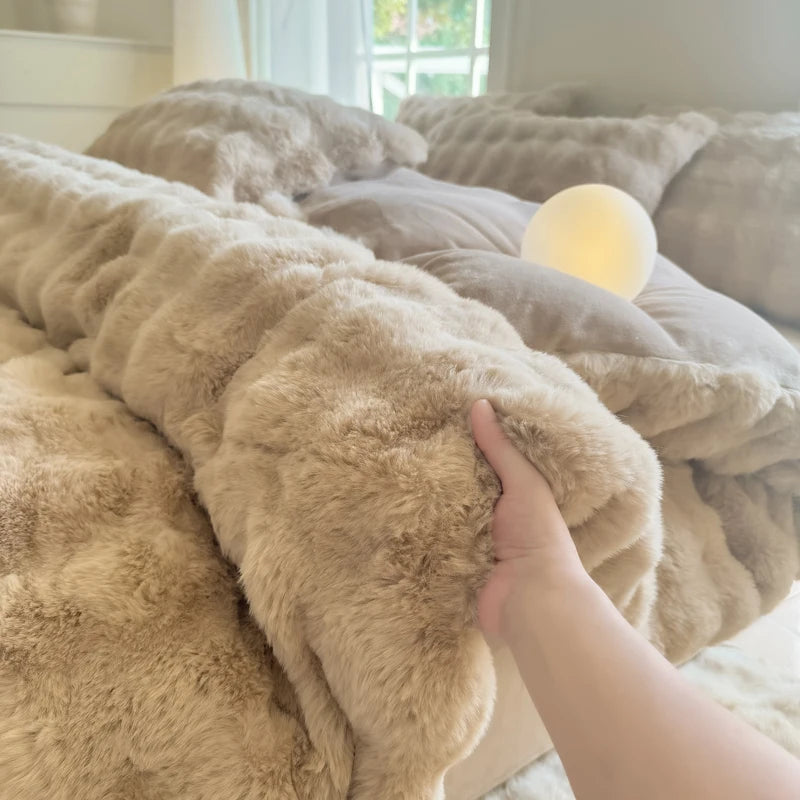 A hand is touching a fluffy beige rabbit fleece duvet cover on a bed.