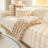 A beige plush rabbit fur sofa cushion cover displayed on a white bed with natural light.