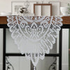White crochet lace table runner with a scalloped edge and tassels displayed on a wooden table.