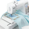A white Brother embroidery machine with a magnetic embroidery hoop and accessories laid out on a light blue cloth.