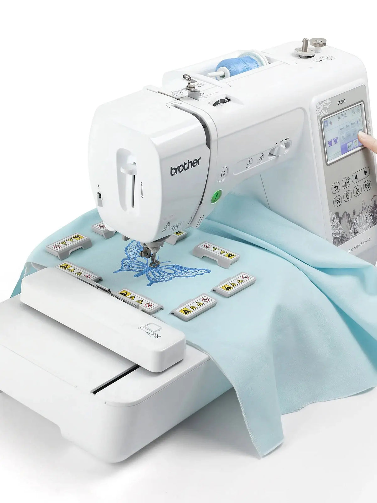 A white Brother embroidery machine with a magnetic embroidery hoop and accessories laid out on a light blue cloth.