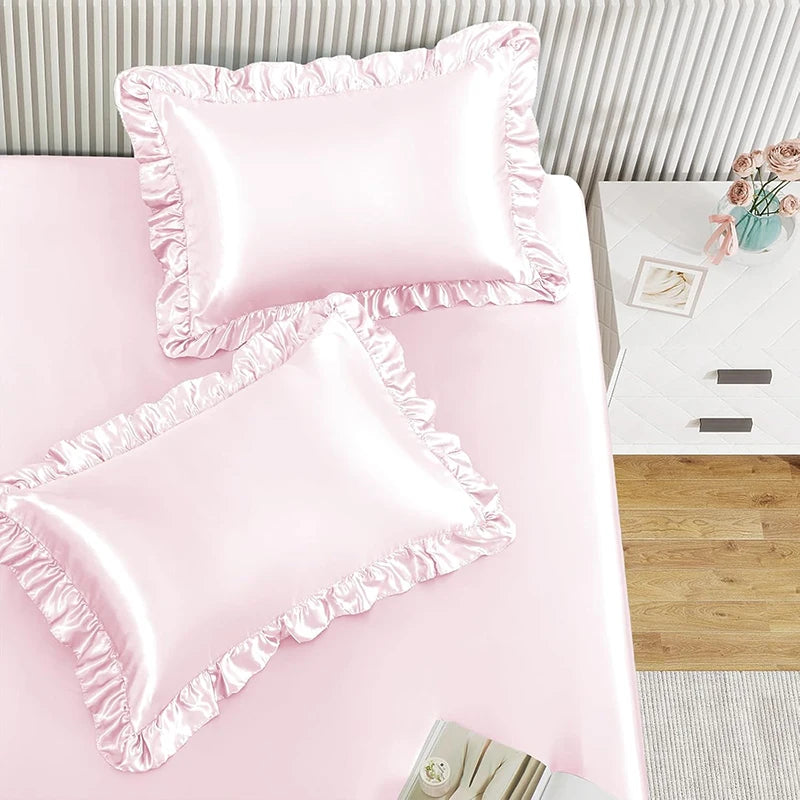 Two pink ruffled satin pillowcases with silky envelope closures displayed on a pink surface.