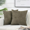 Two olive green corduroy patchwork pillow covers resting on a white sofa with a light throw blanket.