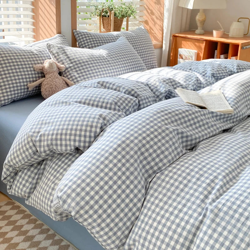 A bed dressed with a blue and white gingham plaid duvet cover, pillowcases, and a stuffed animal.