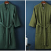 A moss green cotton terry robe hanging on a wooden hanger against a dark blue wall.