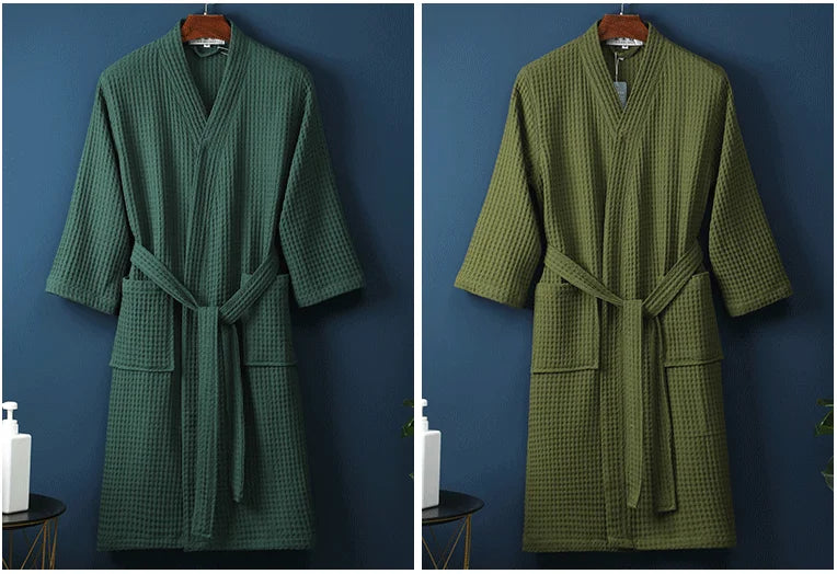 A moss green cotton terry robe hanging on a wooden hanger against a dark blue wall.