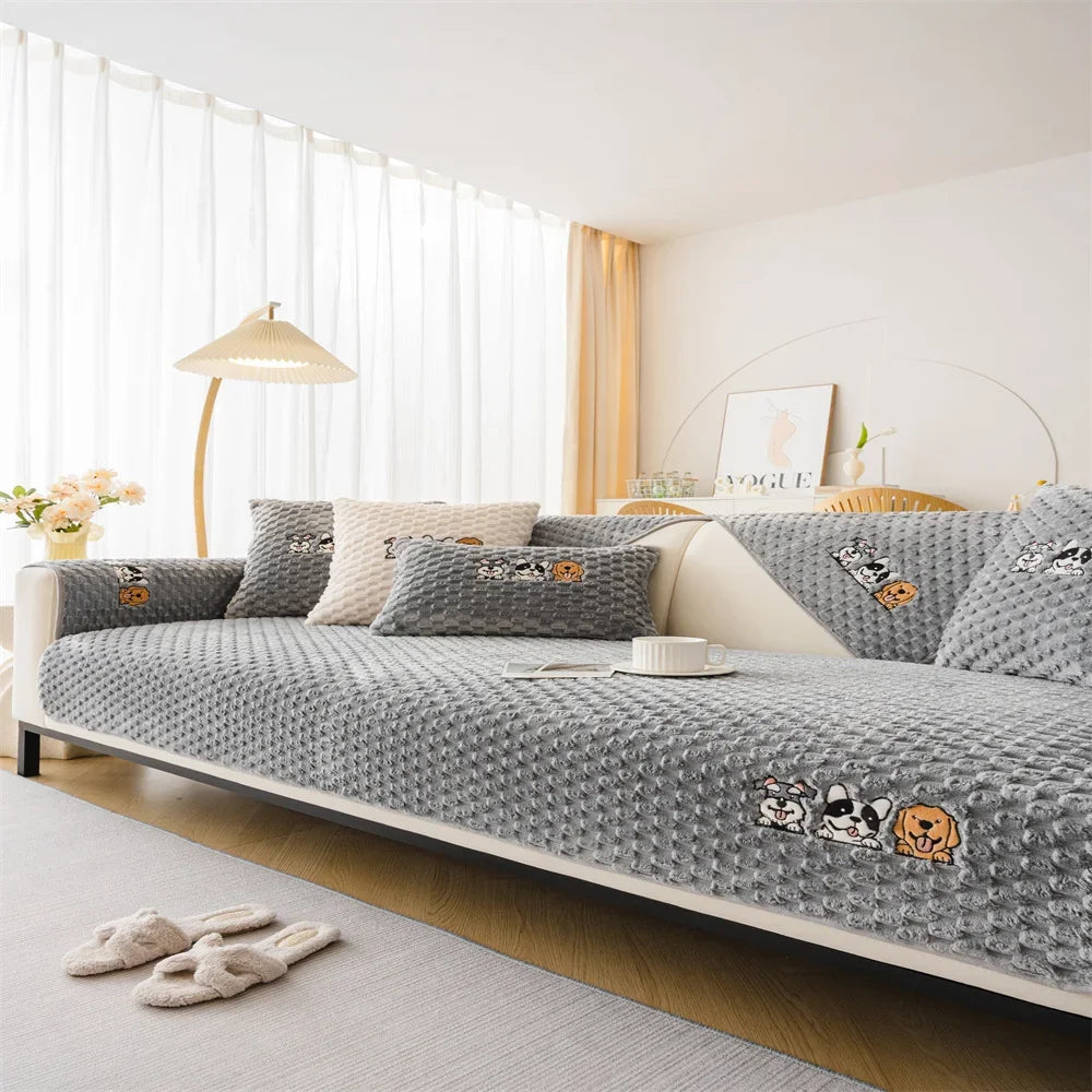 A gray non-slip plush sofa cover with decorative patches is displayed on a light-colored sofa.