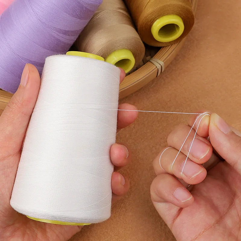 A hand is unwinding white sewing thread from a spool, with several colored thread spools visible in the background.